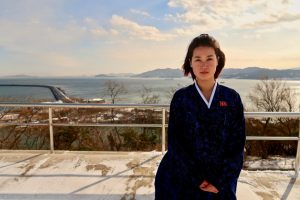 A North Korean tour guide at Nampo, with the sea and headland in the background.
