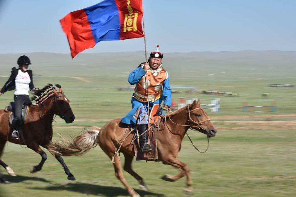 A Mongolian horseman rides past with the flag of Mongolia in the run-up to a Mongol horse race.