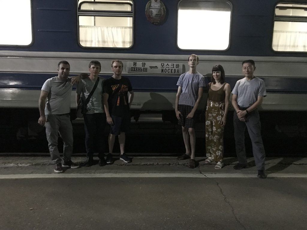 Six tourists stand in front of the Moscow-Pyongyang train carriage.
