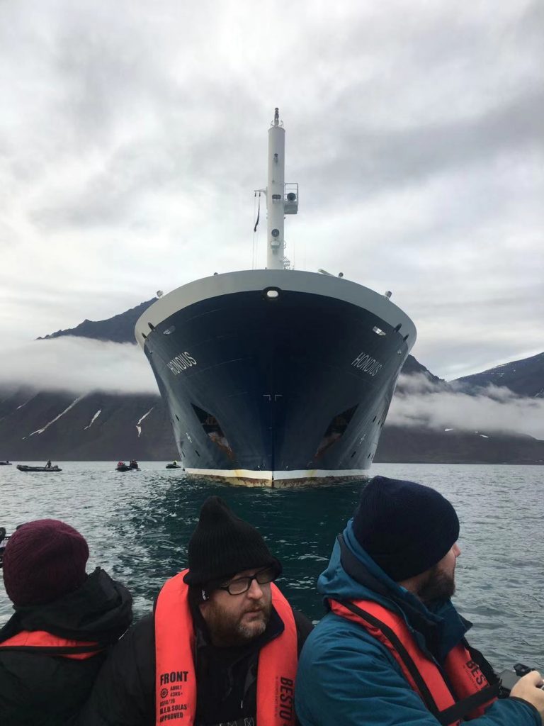 The cruise ship MV Hondius sits in the water behind a group of tourist making landfall in a zodiac (a sturdy rubber dinghy).