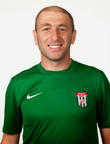 A smiling man with cropped hair poses in a green Abkhazia football jersey.